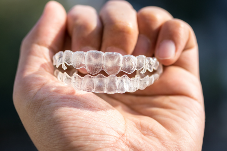 Patient holding clear Vivera retainer after completing Invisalign treatment at orthodontic office